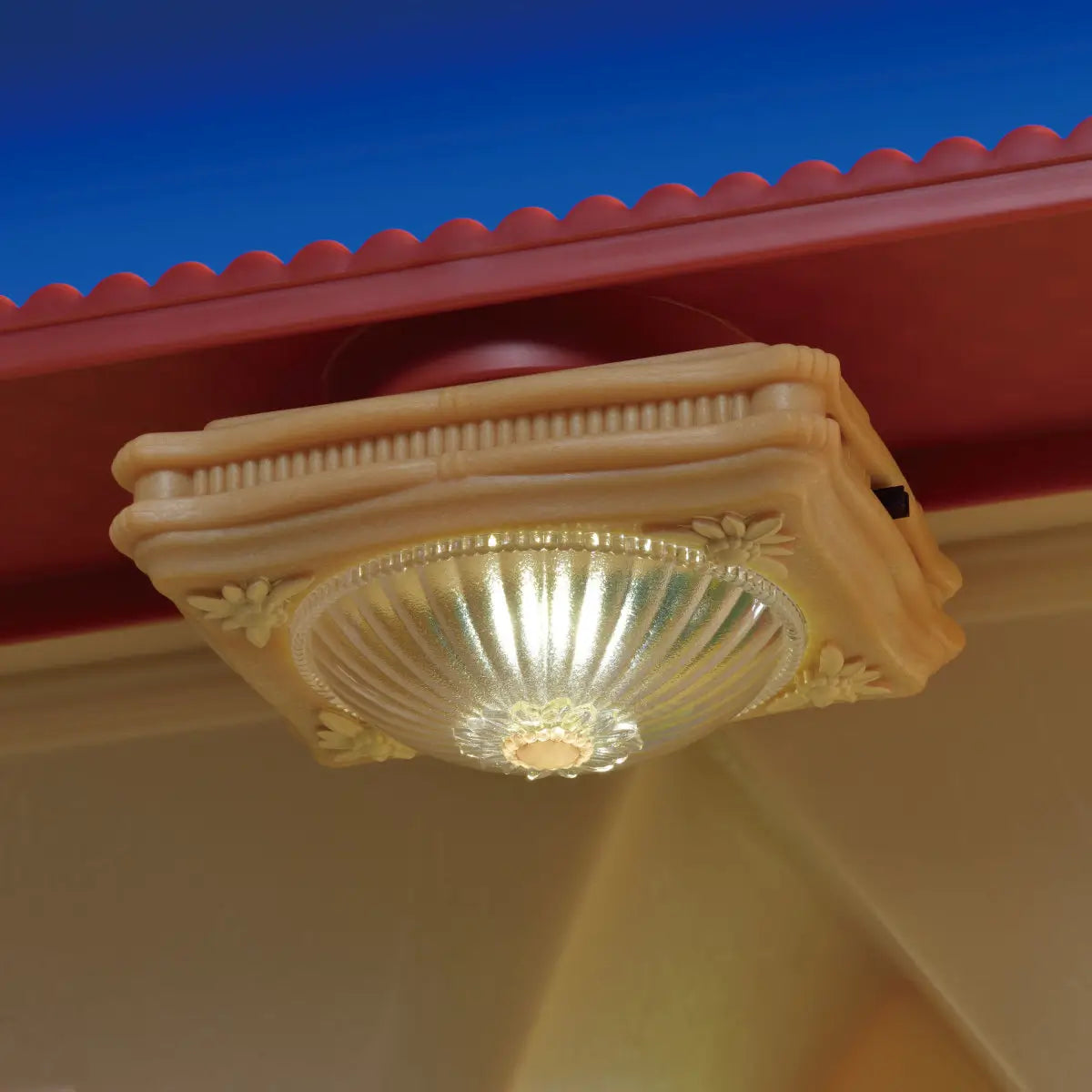 Calico Critters ceiling light accessory attached to a dollhouse ceiling, featuring a translucent ribbed dome shade with floral detailing, emitting a soft yellow glow under a red roof edge.