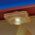 Calico Critters ceiling light accessory attached to a dollhouse ceiling, featuring a translucent ribbed dome shade with floral detailing, emitting a soft yellow glow under a red roof edge.