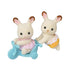 Calico Critters Chocolate Rabbit Twins feature cream flocked fur and brown-tipped pink ears, with one in pink lace and one in yellow lace beside a blue tricycle.
