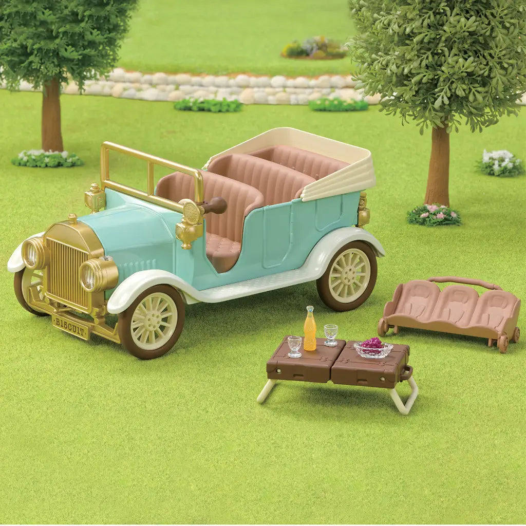 Calico Critters Classic Family Car picnic scene features a mint and gold convertible, tan bench, brown suitcase table, clear glasses, grapes, and drink on green grass.