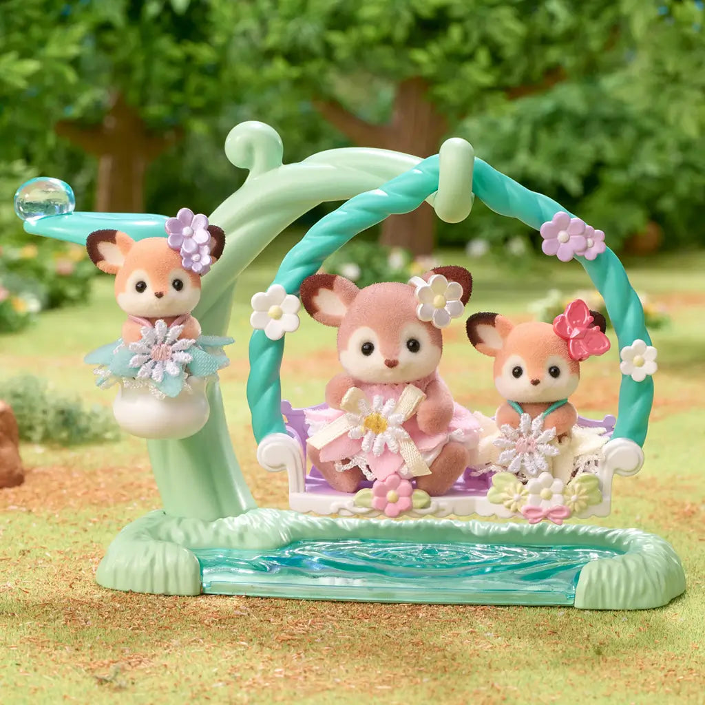 Calico Critters Deer Babies Floral Swing Set with three flocked baby deer in pastel dresses sitting on a green and white swing decorated with flowers, placed outdoors on grassy terrain.