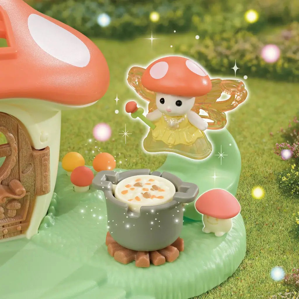 Calico Critters Mushroom Fairy scene shows a cream fairy with an orange cap, translucent wings and yellow dress beside a gray cooking pot and tiny mushrooms in a garden.