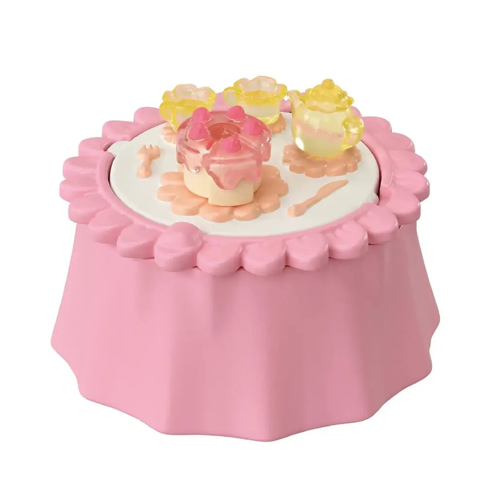 Calico Critters tea table is pink molded plastic with a scalloped flower edge, topped with a cake, translucent yellow cups and dishes, and tiny utensils on white.