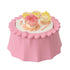 Calico Critters tea table is pink molded plastic with a scalloped flower edge, topped with a cake, translucent yellow cups and dishes, and tiny utensils on white.