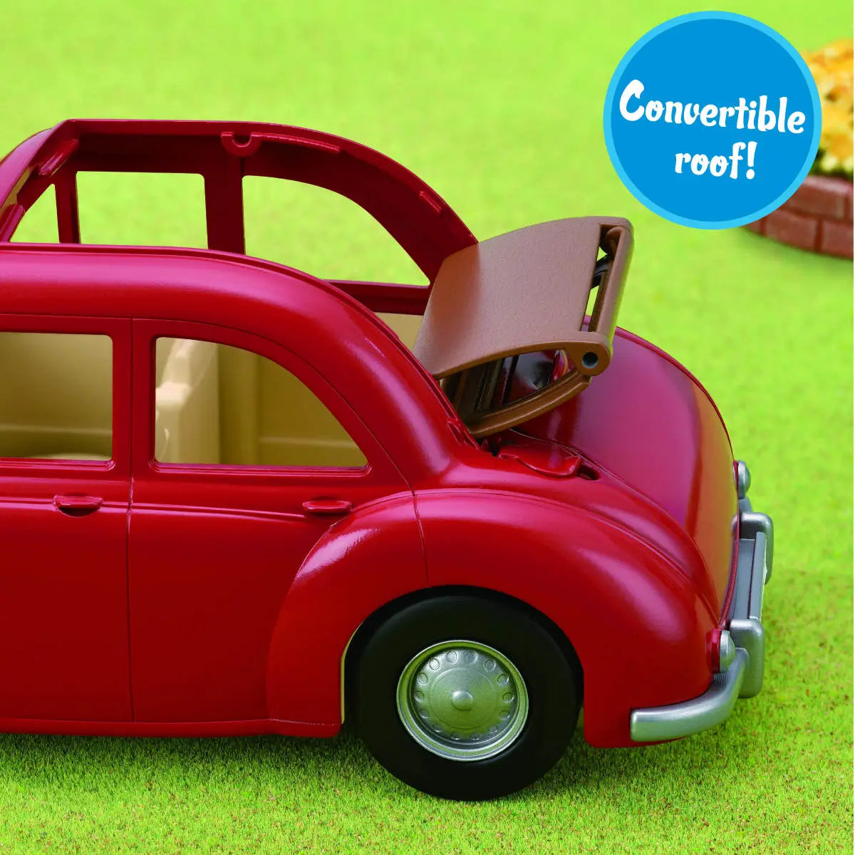 Calico Critters Family Cruising Car close-up showing shiny red toy car with tan convertible roof partially open, displayed on green grass with a label reading “Convertible roof!”