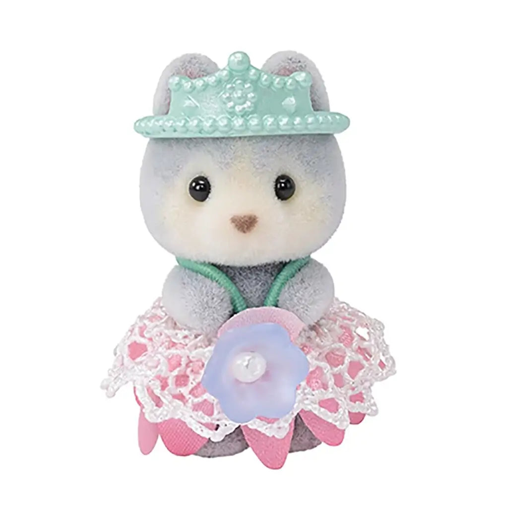 Calico Critters Husky Cradle Baby wears a pastel pink lace skirt and teal tiara-style hat, holding a tiny blue flower accessory while posed upright.
