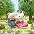 Calico Critters Freya and Theo Anniversary Friends set with cream and tan flocked figures in formal outfits, lace dress with red bow and blue plaid suit, posed in green garden park setting.