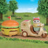 Calico Critters cat figure drives cream scooter with brown seat, towing a large orange burger-shaped food stand trailer topped with a red flag through grassy park scenery.