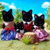 Calico Critters Midnight Cat Family features four black flocked cat figures in colorful fabric outfits gathered around a tree-stump table in a sunny miniature garden.