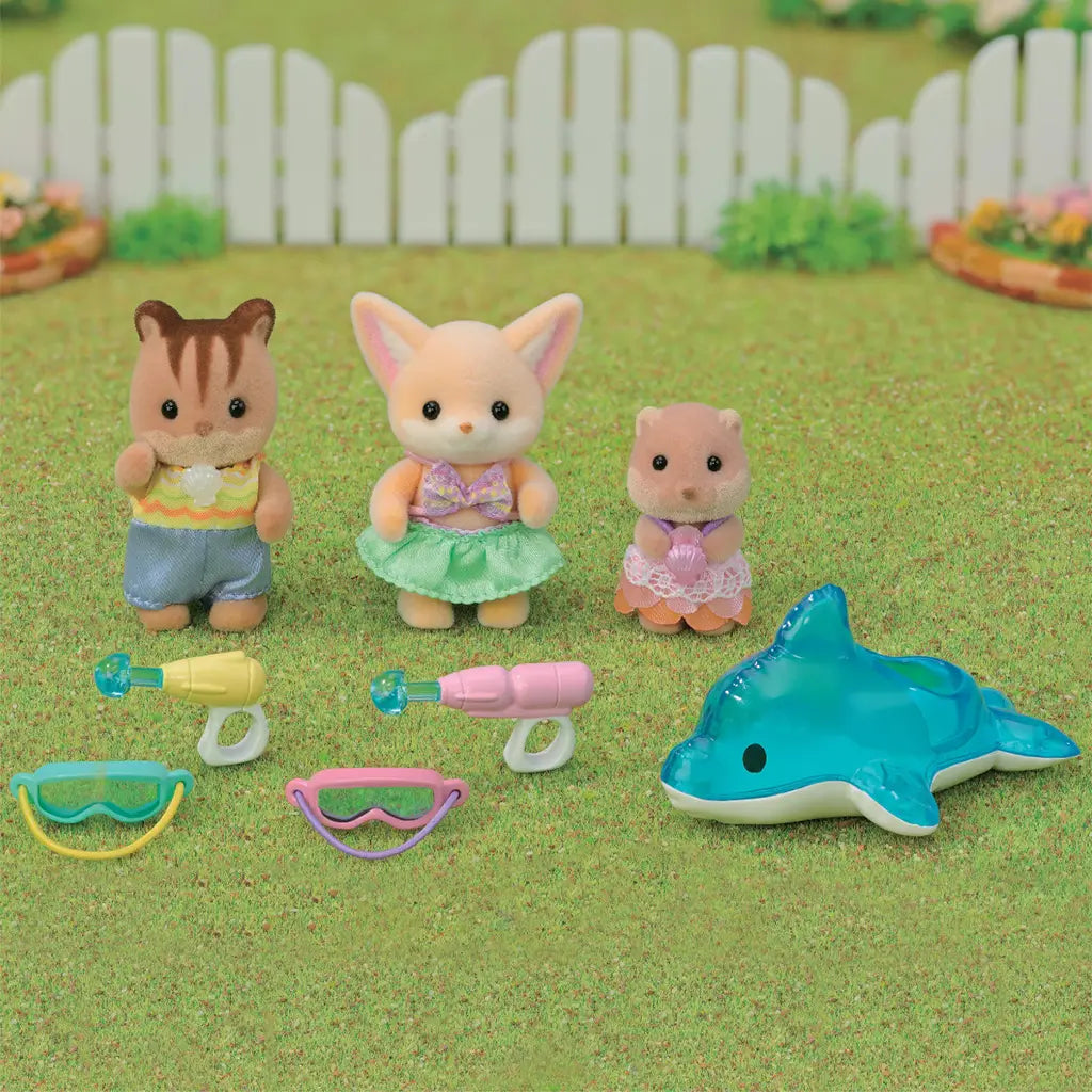 Three Calico Critters animals in swimwear play outdoors on grass with goggles, water blasters, and a blue dolphin float toy, set against a white picket fence.