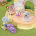 Calico Critters nursery castle playground playset with pastel pink turrets and rainbow arch, shown with baby animal figures playing on a round stage platform and riding a small purple toy train.