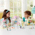 Two smiling children play indoors with Calico Critters Nursery Sandbox & Pool castle, bus, and figures, featuring pastel towers, slides, sandbox, and miniature animal characters.