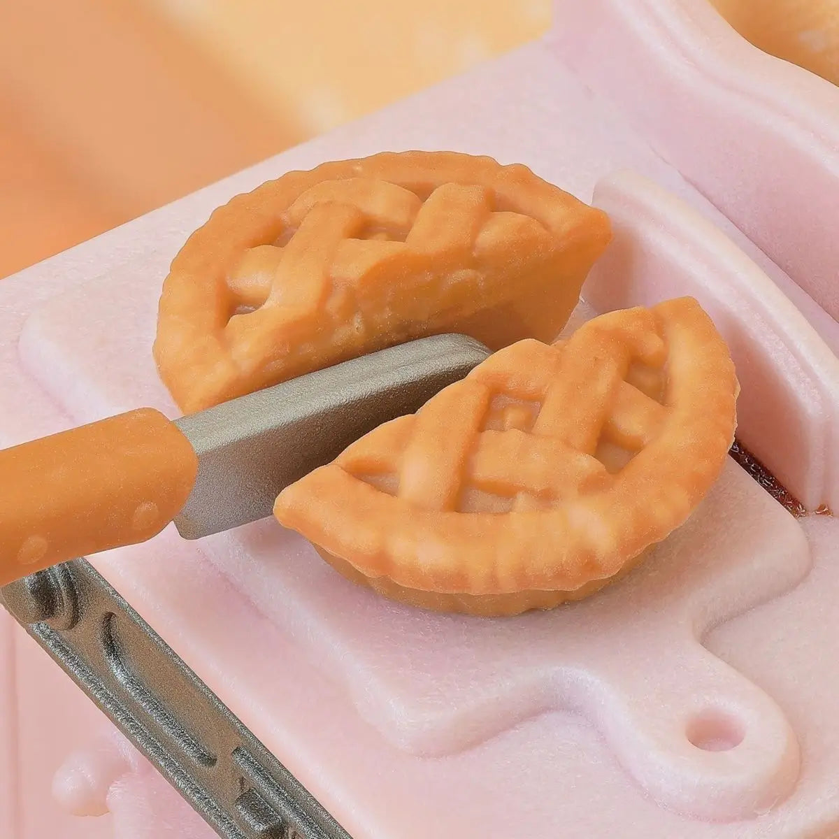 Calico Critters kitchen play scene includes white refrigerator, pink stove and oven, frying pan with pie, bread loaves, and lace curtained window set in yellow dollhouse kitchen.