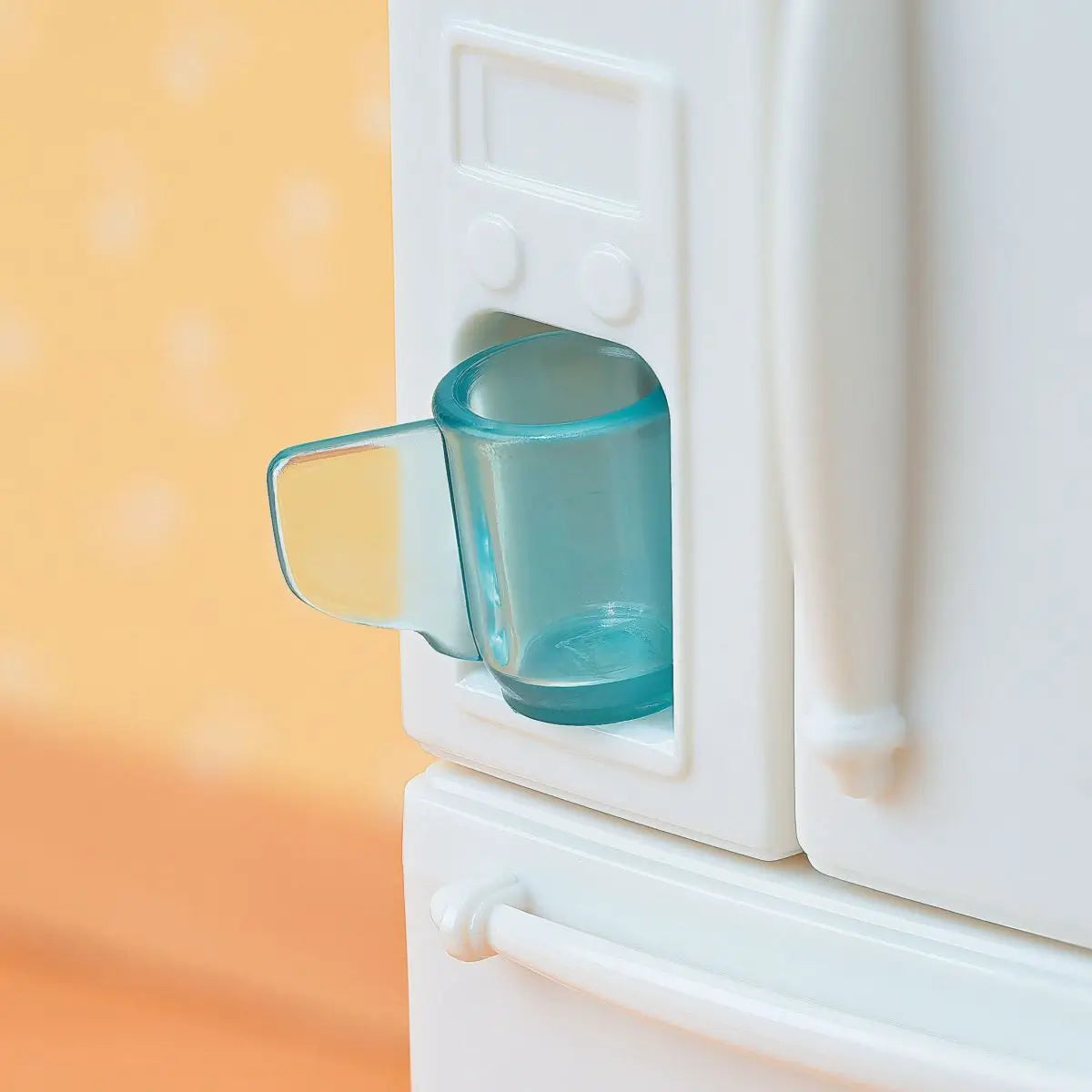 Calico Critters refrigerator water dispenser features white molded plastic door with clear aqua cup inserted in built in ice and water slot against soft orange background.