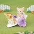 Calico Critters Playtime Castle Nursery outdoor scene with baby figures on a lavender see-saw in a grassy garden, showing playful interaction between a fennec fox and giraffe character.