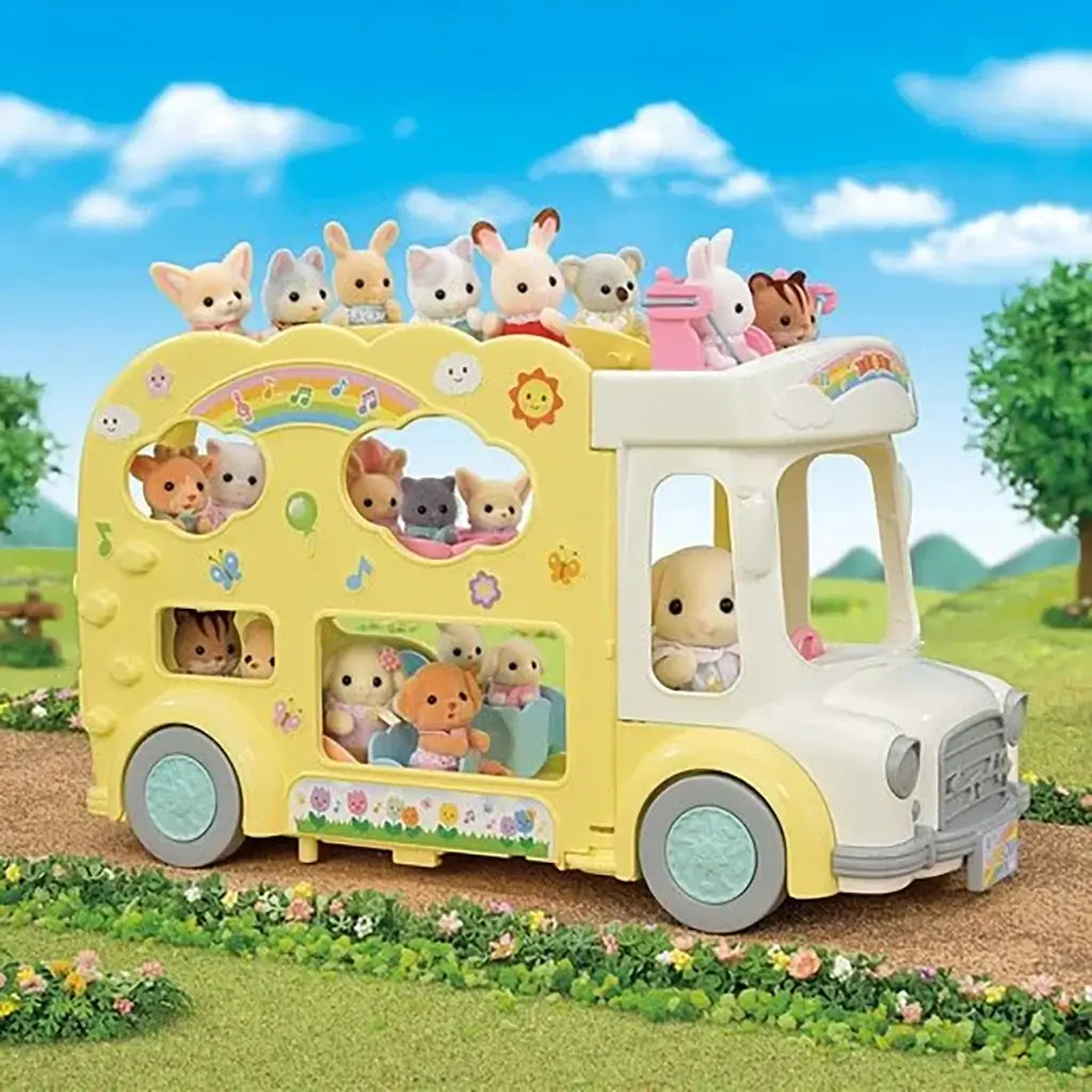 Calico Critters Rainbow Fun Nursery Bus playset outdoors with animal babies riding inside and on top of the yellow pastel bus decorated with clouds and rainbows.
