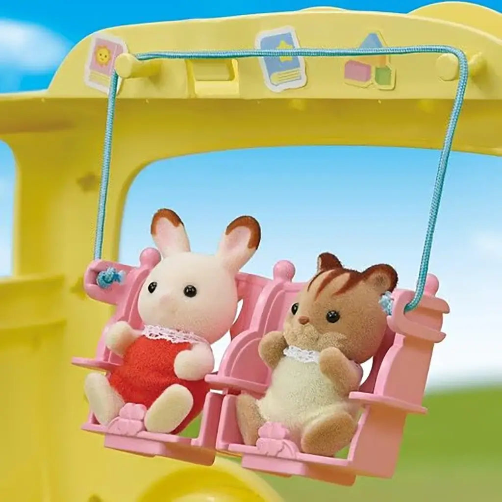 Close-up of Calico Critters rabbit and chipmunk baby figures seated in pink swing attachment inside the yellow Rainbow Fun Nursery Bus toy playset.