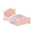 Light pink plastic miniature bed with curved headboard and footboard, featuring a colorful floral-print blanket and white lace trim, part of the Calico Critters cozy cottage furniture collection.