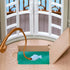 Calico Critters fishing rod in brown plastic curves over a turquoise water feature, with a pale blue fish on the line beside an open hatch and white arched doors.