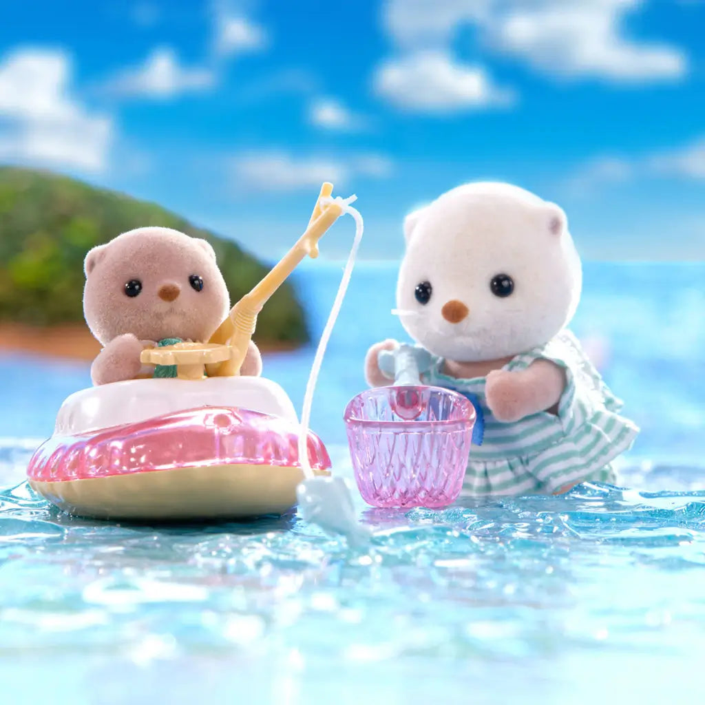 Calico Critters Sea Otter Sisters playing in a water fishing scene with one in a small toy boat catching fish and the other holding a pink net, set against a bright blue seaside backdrop.