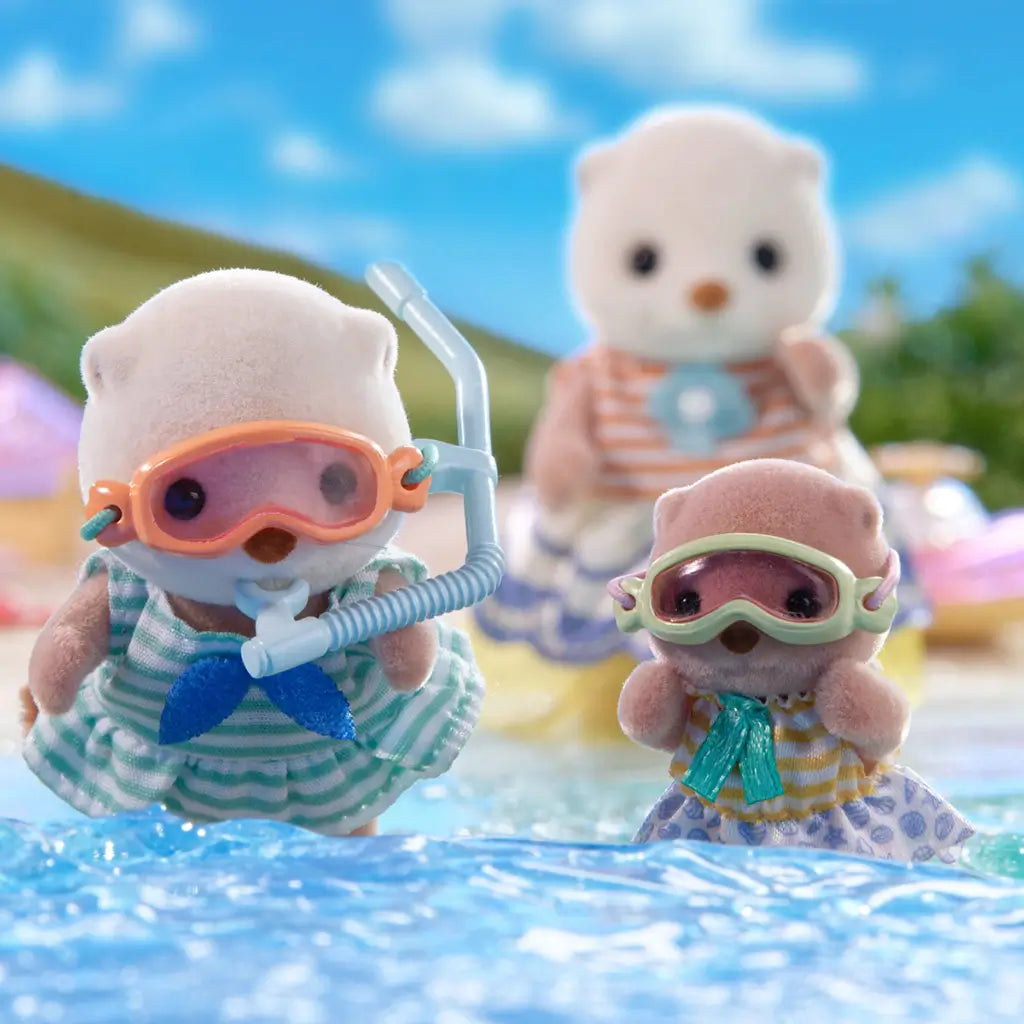 Calico Critters Sea Otter Sisters wearing snorkel masks playing in shallow water, with waves around them and a larger otter figure in the background, under a sunny blue sky outdoors.