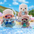 Calico Critters Sea Otter Sisters wearing snorkel masks playing in shallow water, with waves around them and a larger otter figure in the background, under a sunny blue sky outdoors.