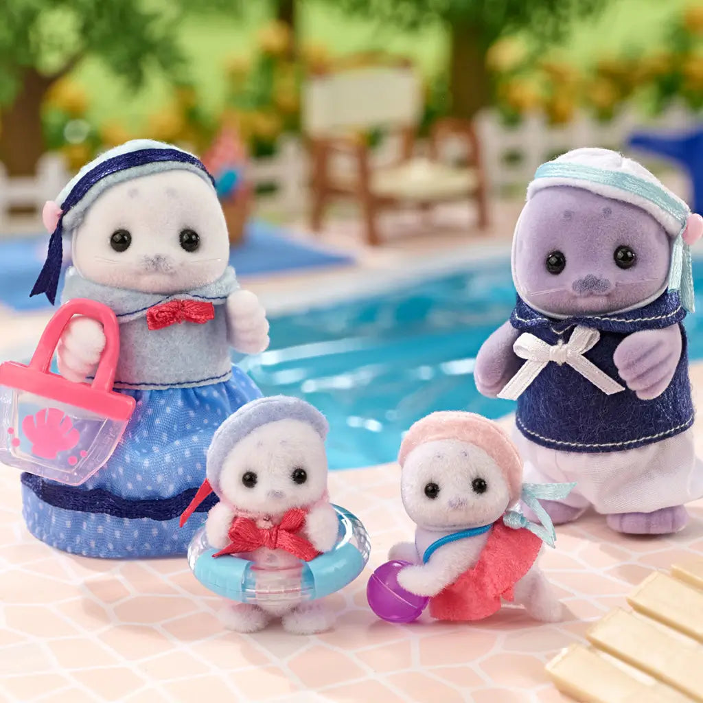 Calico Critters Seal Family toys arranged by a swimming pool scene, including mother, father, and two baby seals dressed in blue and pink, with basket, tote, and float ring.