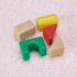 Colorful toy building blocks including red triangle, green arch, yellow cylinder, and beige shapes rest on a soft textured surface, designed for early learning and creative play.