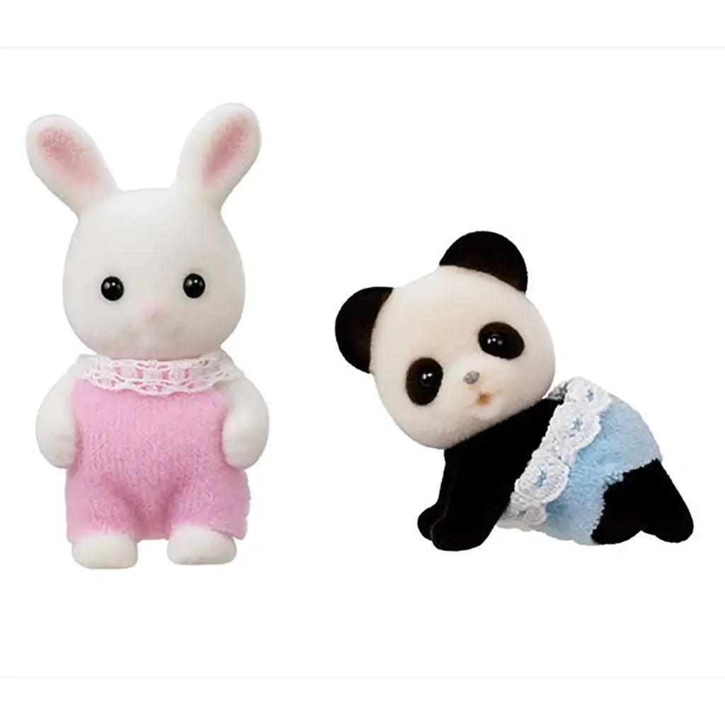 Close-up of Calico Critters snow rabbit baby in pink romper and panda baby in blue diaper with lace trim, both flocked miniature animal figures designed for dollhouse pretend play.