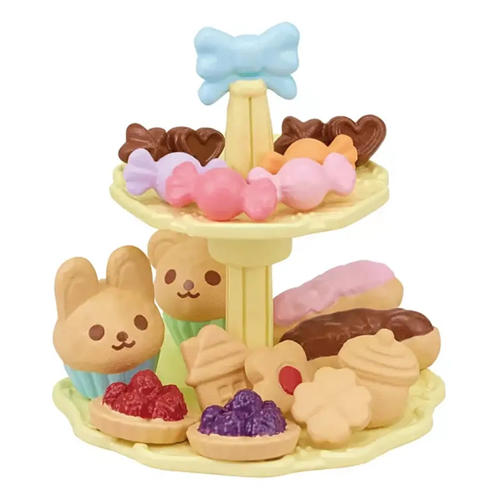 Tiered cake stand from Calico Critters Sweets Party Set holding toy cupcakes shaped like rabbits and bears, tarts, cookies, eclairs, and candy with pastel details.