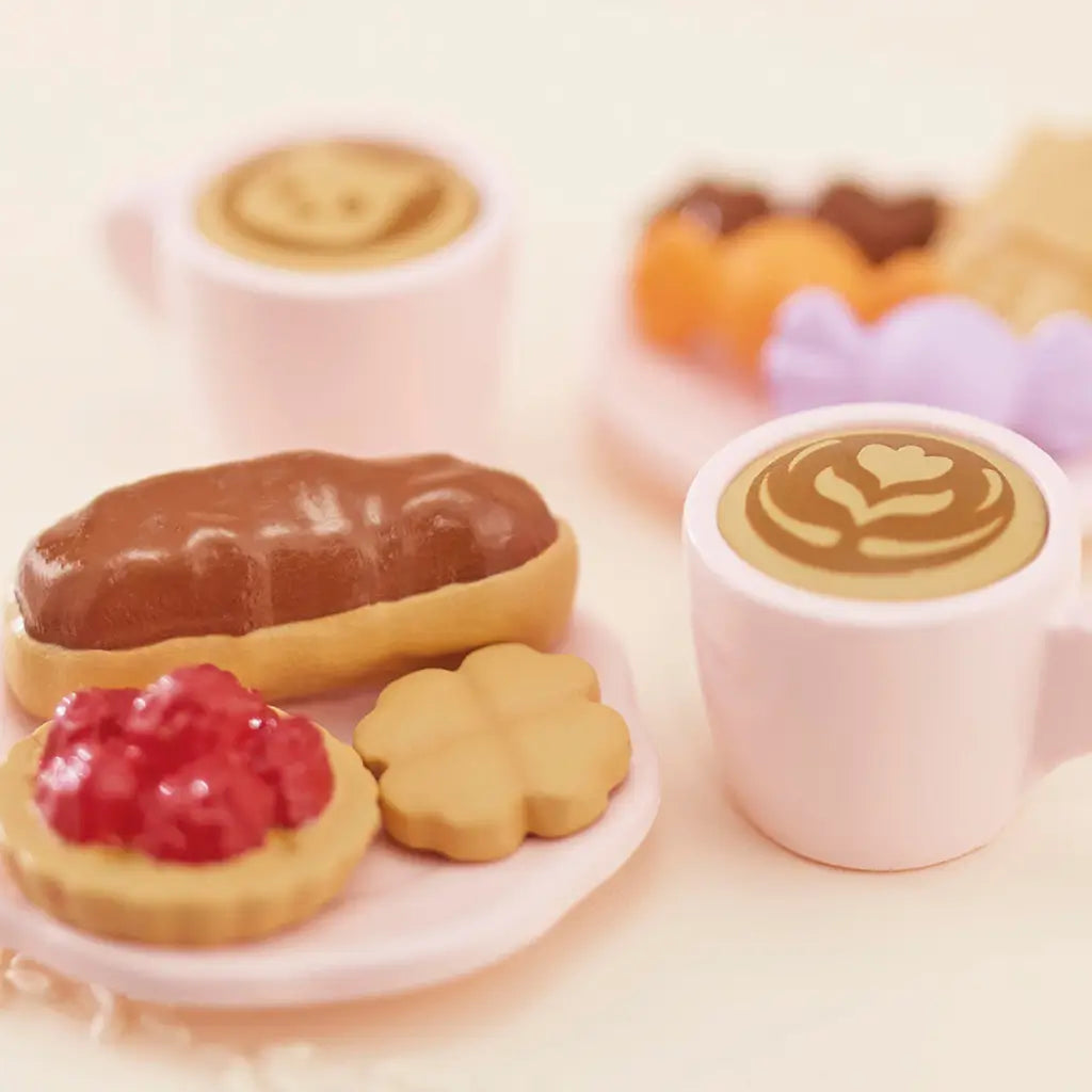 Close-up of Calico Critters Sweets Party Set accessories including latte mugs with foam art, croissant, tart, and assorted pastel cookies on tiny toy plates.