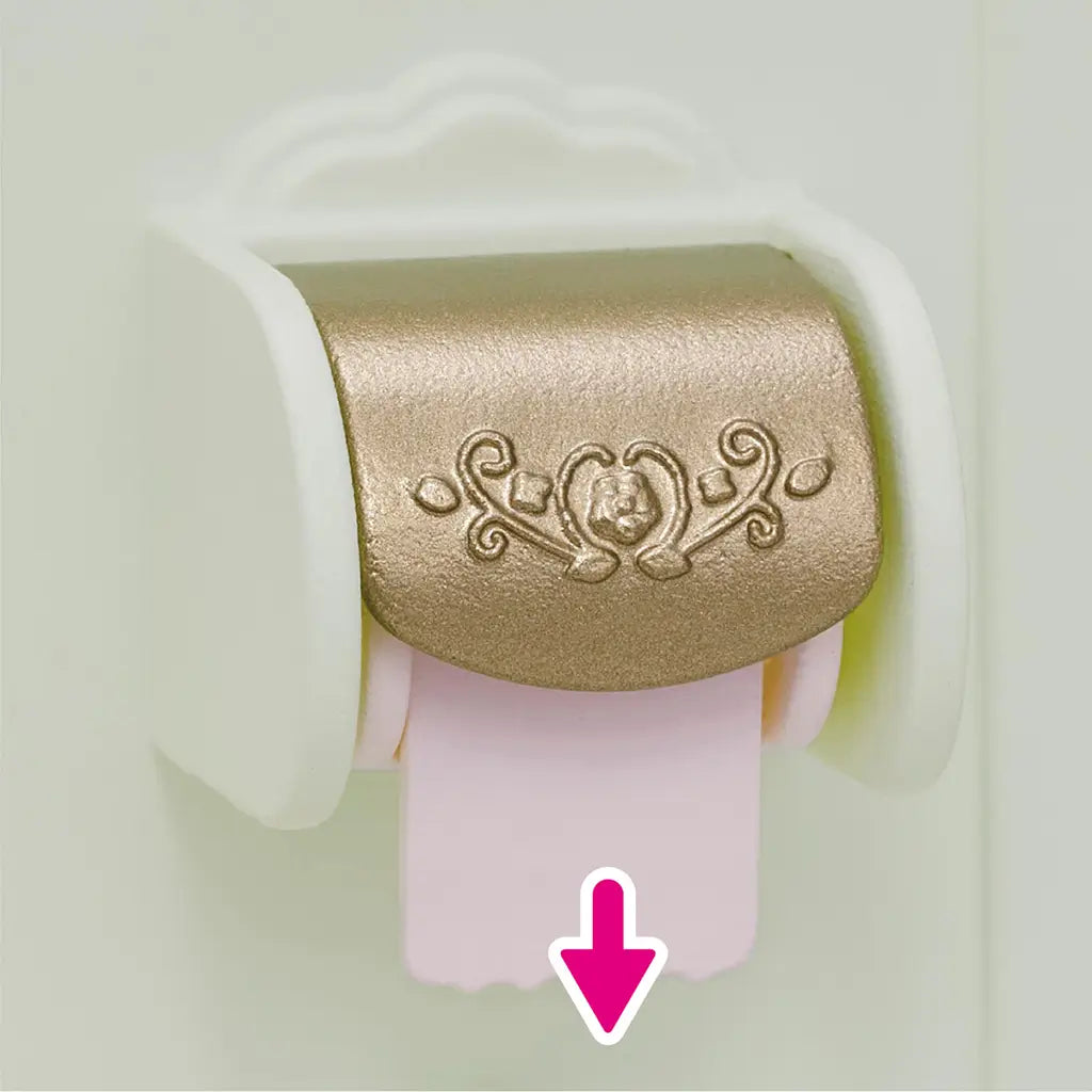 Close-up of Calico Critters Toilet Set toilet paper holder with gold ornate cover, showing pink paper roll being pulled down with arrow indicator.