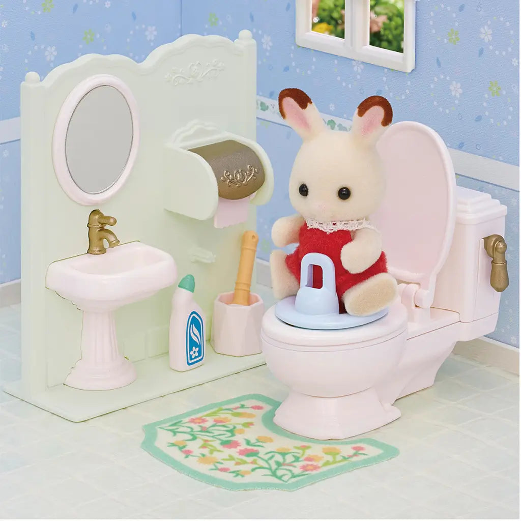 Calico Critters Toilet Set scene with white toilet, sink, floral mat, and small rabbit figure seated, alongside accessories like brush, cleaner, and toilet paper holder.
