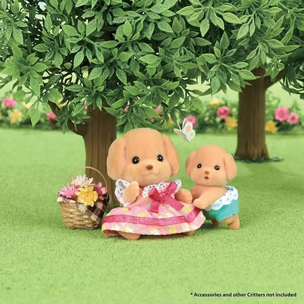 Calico Critters Toy Poodle Twins outdoor play scene shows brown puppy figurine in pink dress with basket of flowers beside twin sibling in diaper under a tree with butterfly.