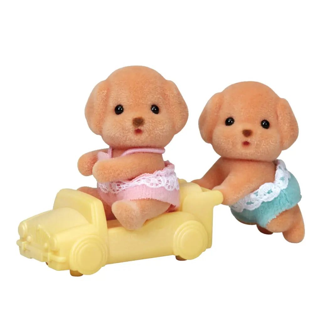 Calico Critters Toy Poodle Twins figurines include two brown puppy characters wearing lace-trimmed diapers, posed with a yellow toy car against a plain white background.