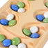 Close-up of a wooden Mancala board with smooth carved pits holding glossy blue, green, and white glass stones, highlighting the tactile texture and natural wood grain detail.