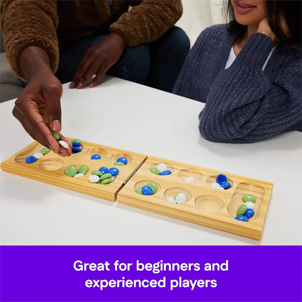 Two players seated at a table playing Mancala with colorful glass stones on a light wooden board, captioned as great for both beginners and experienced players.