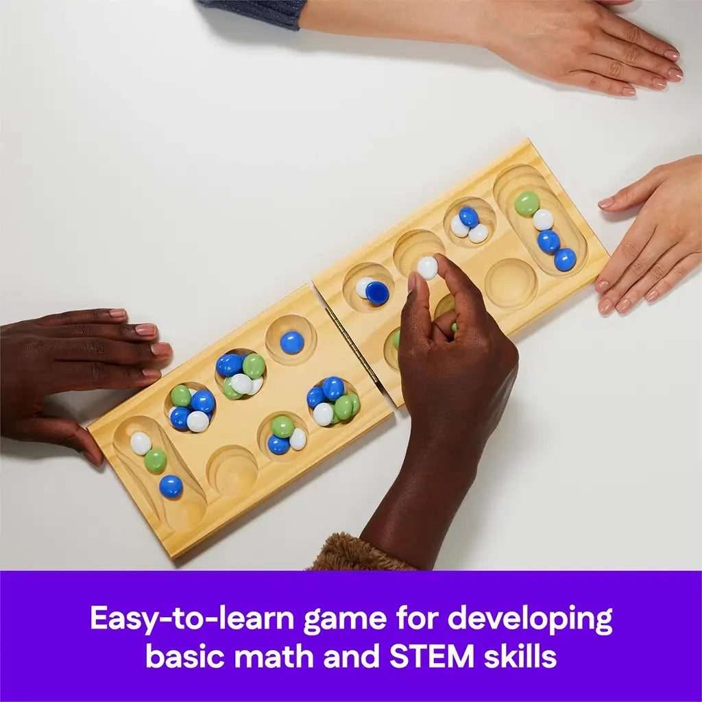 Overhead view of two people playing Mancala, showing hands moving green, blue, and white stones across the board, described as an easy-to-learn game promoting math and STEM skills.