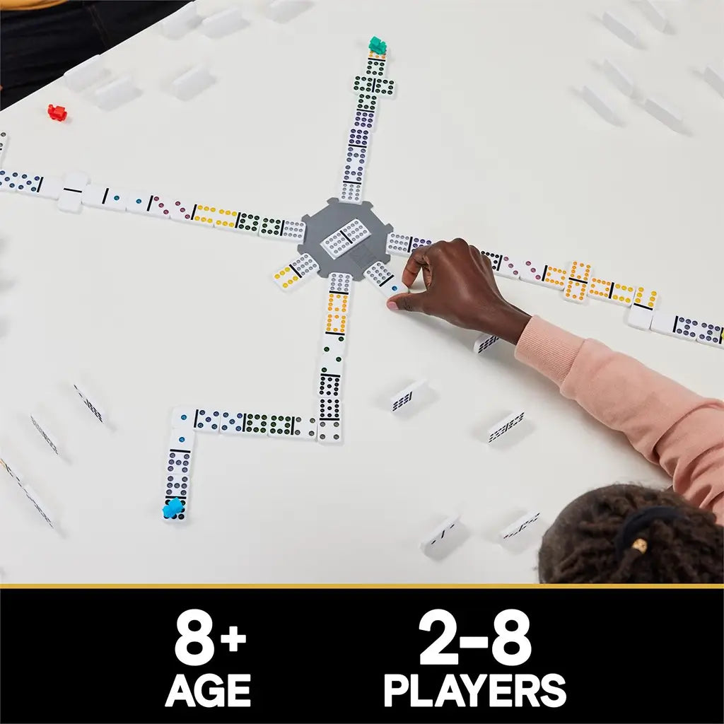 Cardinal Classics Mexican Train Dominoes layout with white tiles forming multiple spokes around a gray hub and colorful train markers, played by several people on a bright white table surface.