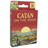 CATAN On the Road card game features red cardboard packaging with yellow title lettering, a stylized island sunset landscape, age 10+ icons, and Asmodee branding.