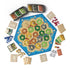 Catan 6th Edition board game components feature a colorful hexagonal island board surrounded by red, blue, yellow, and white pieces, resource cards, dice, and player aids.