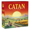 Catan 6th Edition board game box features red cardboard with large yellow Catan title lettering and an illustrated sunset over green fields, mountains, villagers, and sheep.