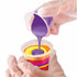Close-up of gloved hands pouring purple paint into a cup layered with yellow, orange, and pink paints, creating a vivid swirl effect ideal for acrylic pour art projects.