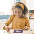 Smiling young girl painting a CreArt axolotl picture at a table, using a brush and pastel paints in a cozy, sunlit room.