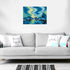 Northern lights painting displayed on a white wall above a gray sofa with decorative pillows, showing how the artwork adds color and atmosphere to the room.