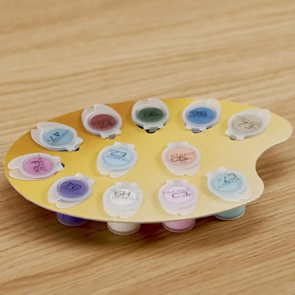 Circular yellow palette card holding twelve numbered acrylic paint pots in pastel shades such as lavender, mint, and peach, part of the Ravensburger CreArt castle kit.