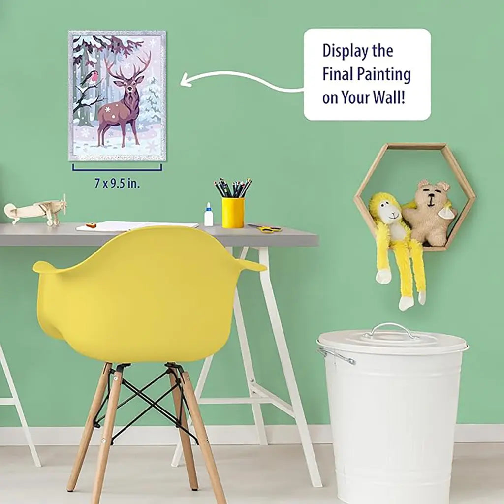 Ravensburger CreArt festive friends paint by numbers kit displayed on a green wall above a modern desk, featuring finished deer and bird winter painting in glitter frame.