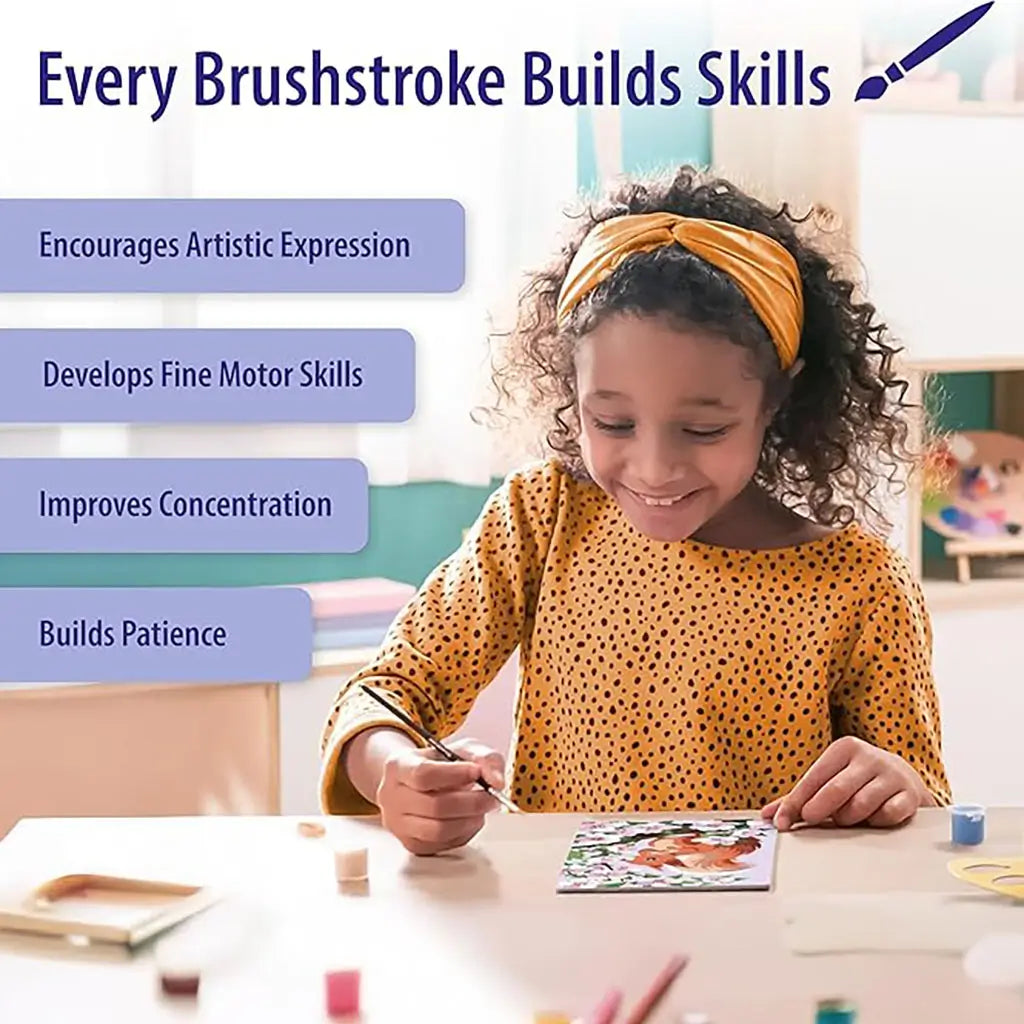Child in yellow headband and polka dot dress smiling while painting with Ravensburger CreArt kit, surrounded by brushes and paint pots, building creativity and patience.