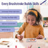 Child in yellow headband and polka dot dress smiling while painting with Ravensburger CreArt kit, surrounded by brushes and paint pots, building creativity and patience.