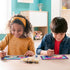 Two smiling children sit at a wooden table painting colorful unicorn by numbers artworks with paint pots, brushes, and playful designs in a bright turquoise playroom.